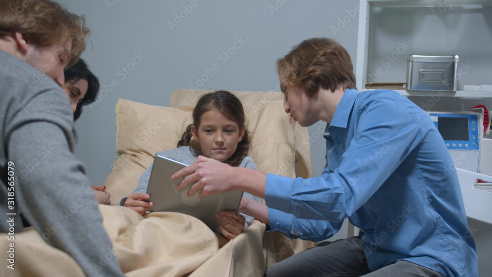 Obraz premium Side view, boy show something on tablet to girl who lie on the bed in the hospital