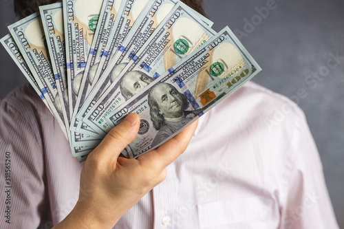 a man hides his face behind a fan of dollar bills