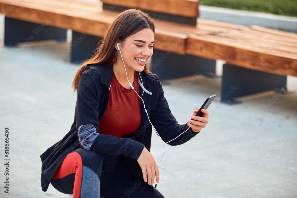 Modern young woman with cellphone making pause during jogging / exercise.