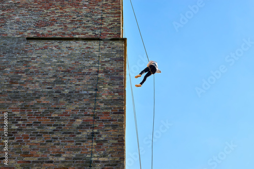 Fototapete Young woman in silhouette, abseiling from a large old tower against a blue sky