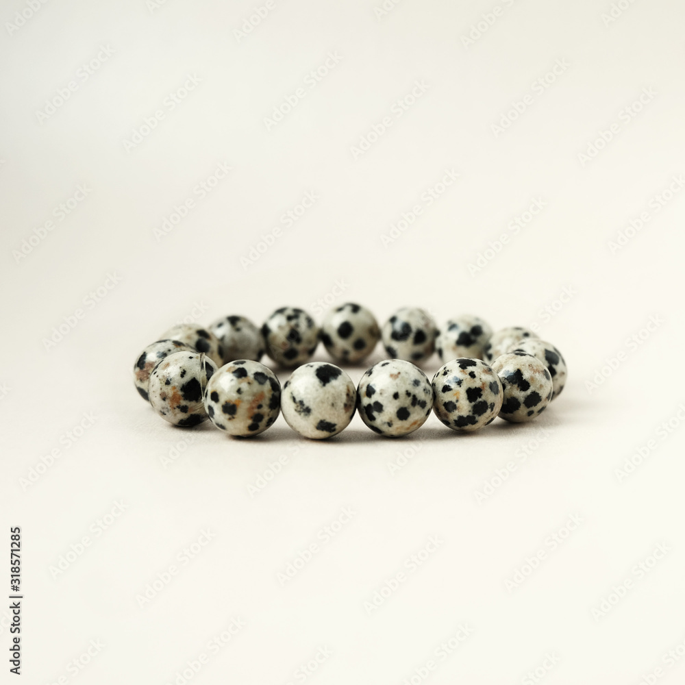 Obraz premium Handmade gem stone dalmatian jasper bracelet decoration product cream lies golden background. Fashion accessory bead stringing hand decoration.
