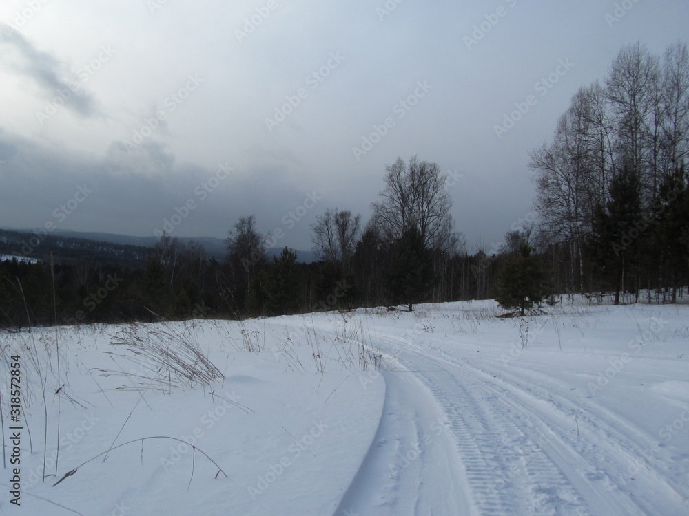 View from the meadow on top of the hill on a cloudy winter day. Dramatic sky. The road leading down. Winter snowy landscape. The nature of Siberia. View from the meadow on top of the hill on a cloudy winter day. Dramatic sky. The road leading down. Winter snowy landscape. The nature of Siberia.