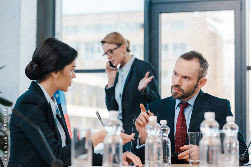 selective focus of diplomats talking and gesturing near businesswoman using smartphone selective focus of diplomats talking and gesturing near businesswoman using smartphone