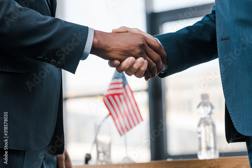 cropped view of multicultural diplomats shaking hands near flag of america photo