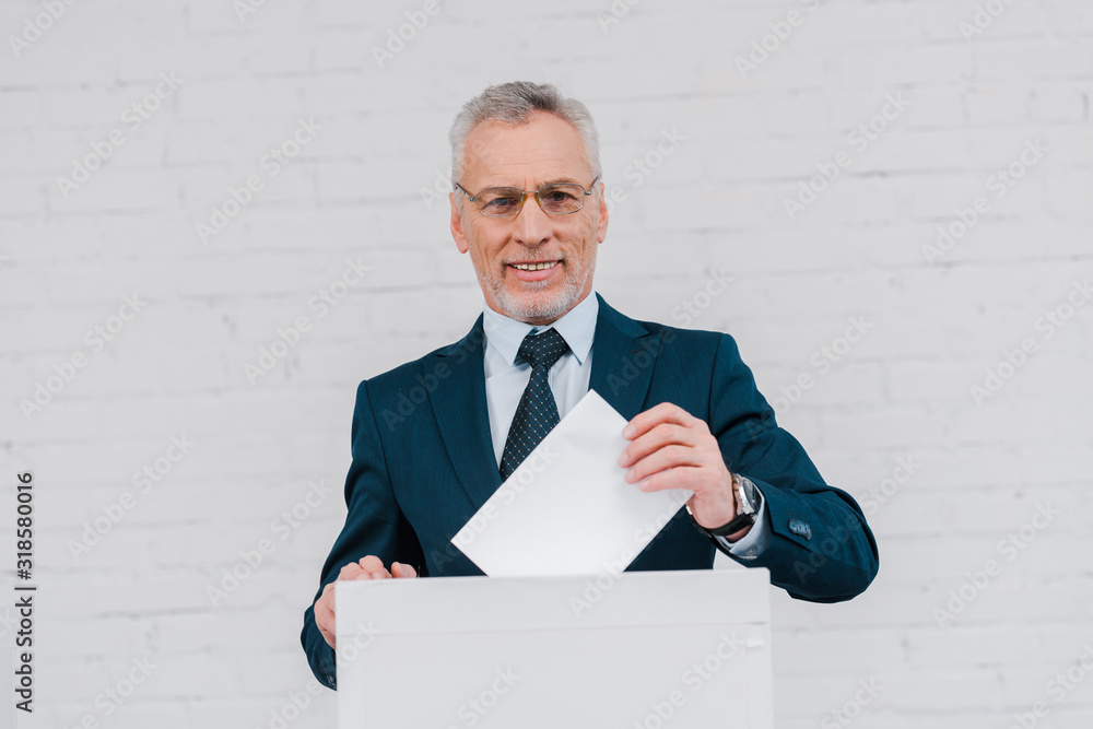 cheerful businessman in glasses voting near brick wall