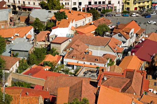 Top view of the old quarter of the city of Tbilisi, Georgia. Many different roofs, houses and windows in one frame. Large green trees are visible between the houses. Nice sunny hot day in the city