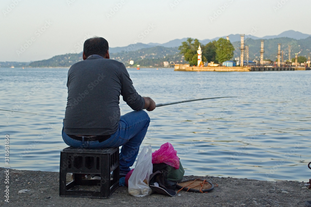 Φωτογραφία A lone fisherman rests on the shores of the city bay with a fishing rod in his hands