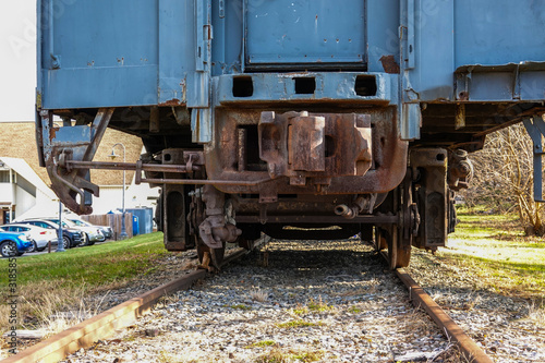 Back view of a blue railroad car on tracks. The car coupler mechanism and undercarriage are rusted