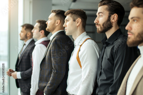 side view on young caucasian bearded business guys looking side at panoramic window, everyone in stylish elegant suits after business conference. isolated in modern office