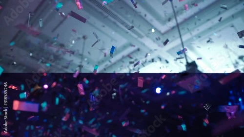 Shine silver confetti fall against blurry illuminated stage in night club slow motion