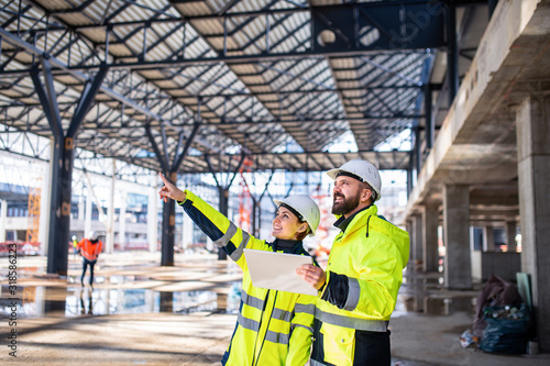 Engineers standing outdoors on construction site, holding tablet.