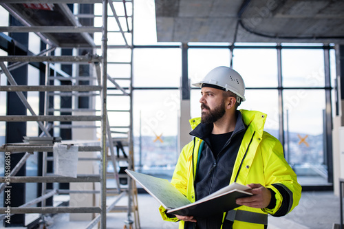 Fotografia Man engineer standing on construction site, holding blueprints.