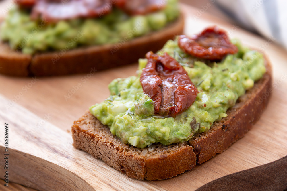 Vegetarian food. Rye bread with guakomole, avocado pasta and dried tomatoes, on wooden cutting board. Avocado toast.