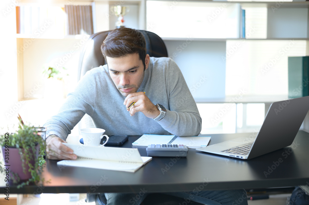 A young man working at a desk with a laptop. Calculator, notepad, pencil, pen and cup of coffee on the side. A young man working at a desk with a laptop. Calculator, notepad, pencil, pen and cup of coffee on the side.