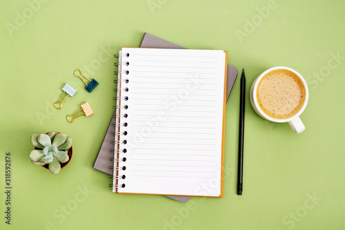 Open notebook with empty page and coffee cup. Table top, work space on green background. Creative flat lay. photo