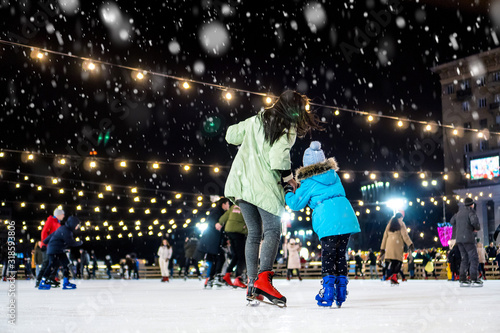 Street skating rink. Mom with daughter at the ice rink. It snows.
