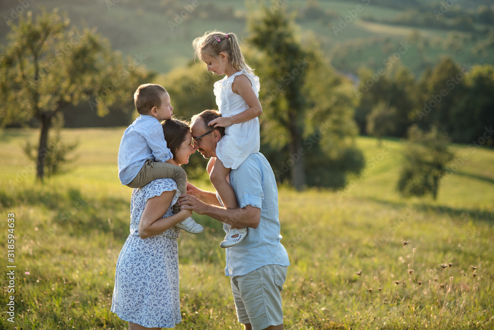 Young family with two small children standing on meadow outdoors at sunset.