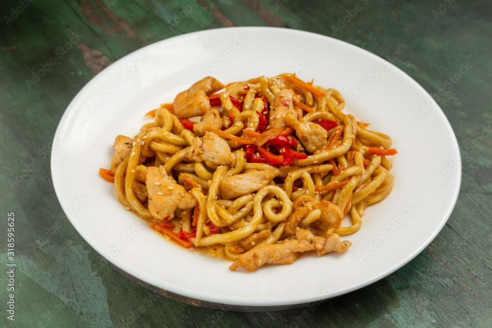 Wok noodles with meat and vegetables in a white plate on a wooden background