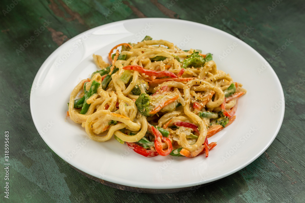 Wok noodles with meat and vegetables in a white plate on a wooden background