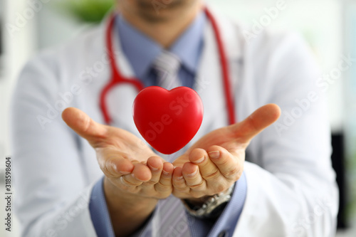 Male medicine doctor hands holding and covering red toy heart photo