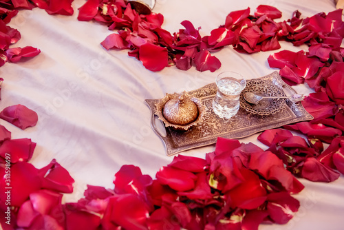 A heart of red rose leaves on a bed and a coffee tray. photo