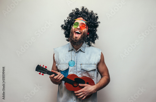 Friendly bearded young male hippie with curly hair in stylish sunglasses plays ukulele guitar isolated on white background photo