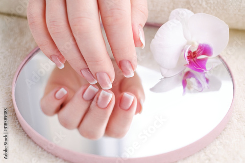 Nails with french manicure. Beautiful female hands with an orchid. Well-groomed skin and nails. Beauty and health concept.