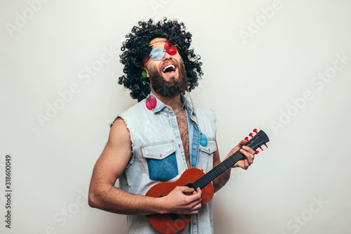 Friendly bearded young male hippie with curly hair in stylish sunglasses plays ukulele guitar isolated on white background photo