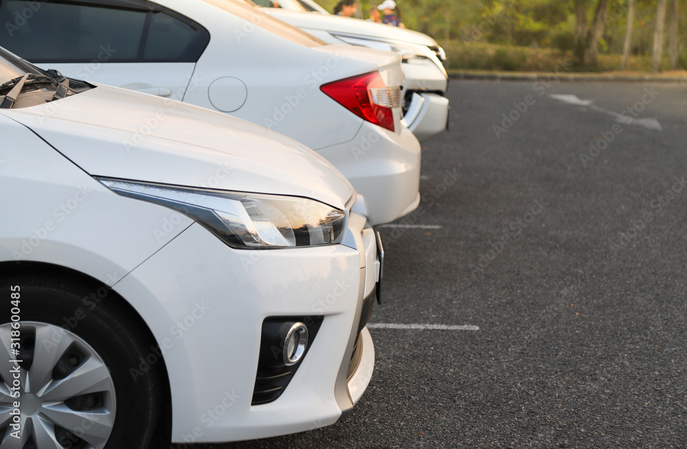 Closeup of front side of white car and other cars parking in outdoor parking lot in the evening. 