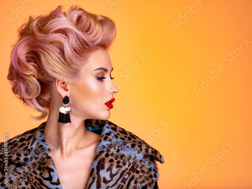 Beautiful woman with style hairstyle. White woman with bright colored makeup. Fashionable young woman is in the spotted fur coat. Stunning blonde girl. Bright eye makeup. Attractive sexy model poses