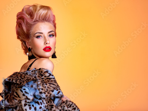 Beautiful woman with style hairstyle. White woman with bright colored makeup. Fashionable young woman is in the spotted fur coat. Stunning blonde girl. Bright eye makeup. Attractive sexy model poses photo
