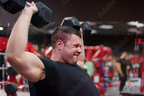 Hard Core Bodybuilding. Muscular athletic bodybuilder fitness model training arms with dumbbells in gym. Concept sport photo of exercises in gym