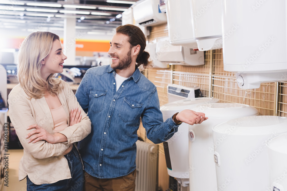 smiling boyfriend and girlfriend talking near boilers in home appliance store smiling boyfriend and girlfriend talking near boilers in home appliance store