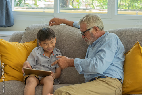 Grandfather and grandson using a tablet on living room, Sernior man teaching grandson workhome by digital tablet, Education concept