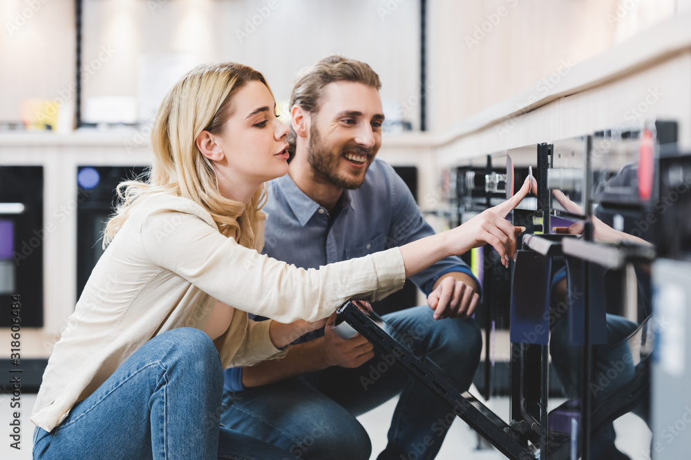 Woman using oven and smiling consultant looking at it in home appliance store Woman using oven and smiling consultant looking at it in home appliance store