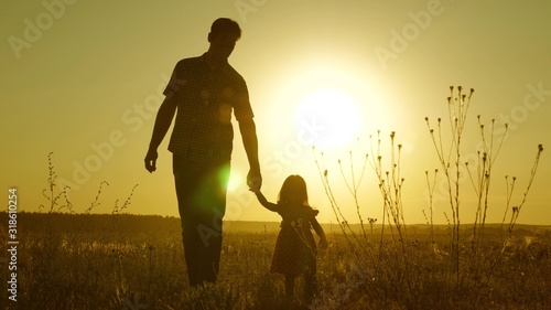 child holds father s hand. dad and baby are resting in park. child plays with his father. little daughter and dad walk around field holding hands. family walks in evening out of town.