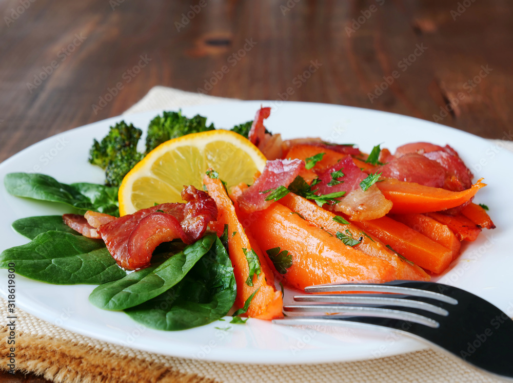 Baked sweet potato wedges with fried bacon bits, baby spinach, broccoli and lemon on plate Baked sweet potato wedges with fried bacon bits, baby spinach, broccoli and lemon on plate
