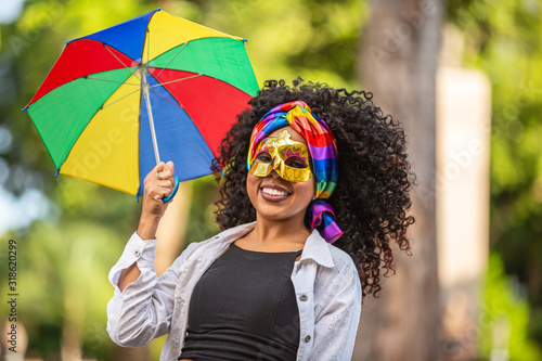 Young curly hair woman celebrating the Brazilian carnival party with Frevo umbrella on street.