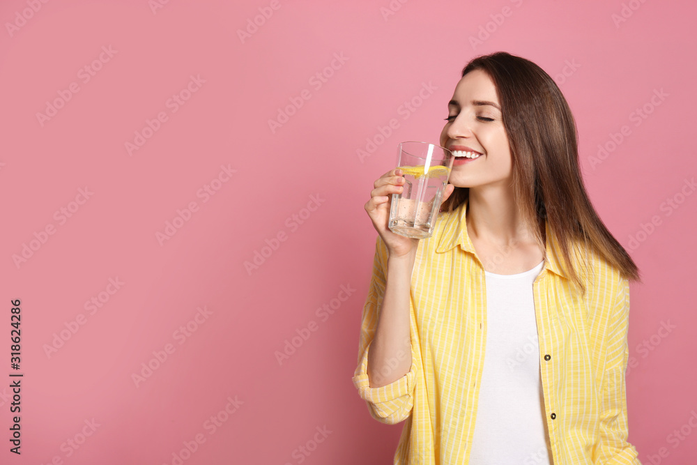 Young woman drinking lemon water on pink background. Space for text Young woman drinking lemon water on pink background. Space for text