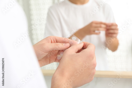 Teen guy using acne healing patch near mirror indoors  focus on hands