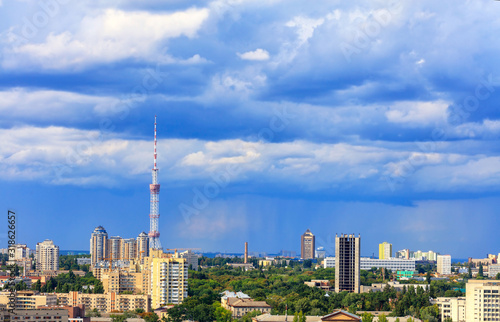 TV tower and residential areas of Kyiv at noon against the backdrop of a stormy blue summer sky.