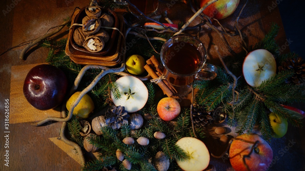 tea in glass mugs in the cold season among sticks of cinnamon, nuts, quince, apples and spruce branches on a wooden table on a black background