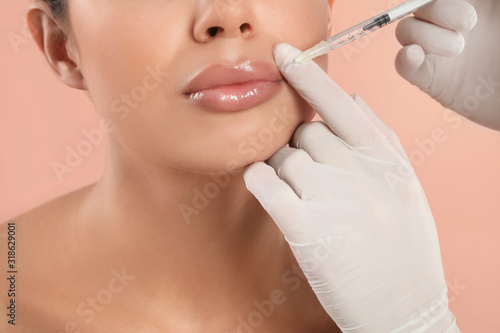 Young woman getting lips injection on peach background  closeup