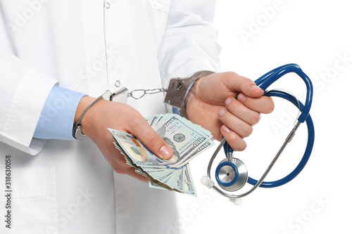 Doctor in handcuffs with bribe and stethoscope on white background, closeup. Corrupted medicine