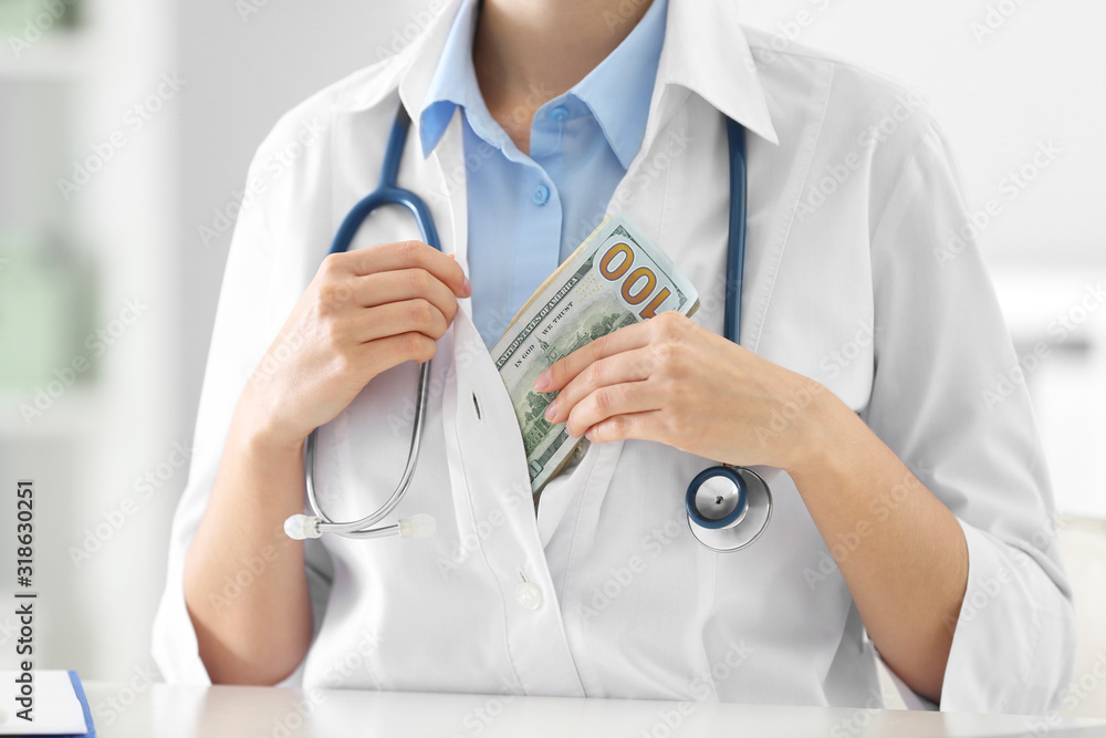 Doctor putting bribe into pocket at desk in clinic, closeup. Corrupted medicine Doctor putting bribe into pocket at desk in clinic, closeup. Corrupted medicine