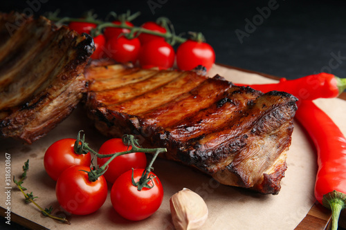 Tasty grilled ribs with tomatoes and peppers on table, closeup