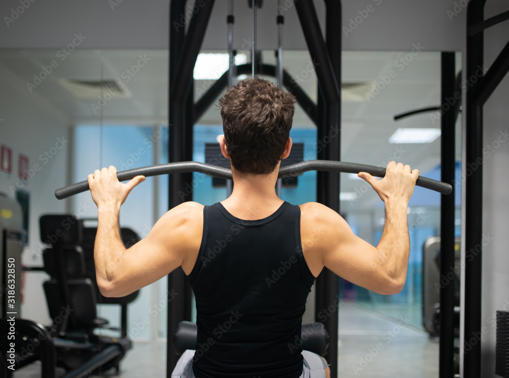 Man using a lat machine in a gym to train his shoulders and back Man using a lat machine in a gym to train his shoulders and back