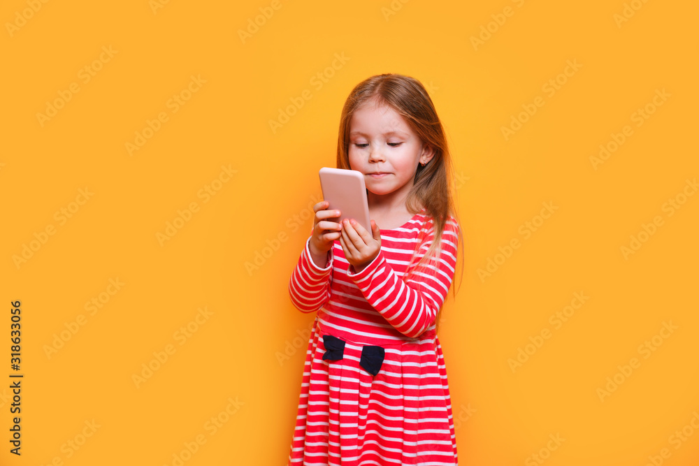 Photo of pretty small girl holding telephone hands making new instagram post on yellow background Photo of pretty small girl holding telephone hands making new instagram post on yellow background
