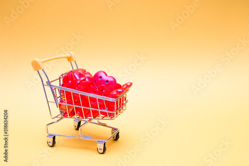 toy shopping trolley full of red hearts and a sweetheart on a yellow background, place for copy, shopping for a holiday, congratulation on Valentine's Day, shopping for a holiday