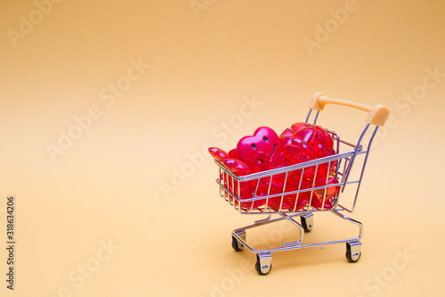 miniature grocery shopping trolley full of red hearts on a yellow background, place for copy, shopping for a holiday, congratulation on Valentine's Day, shopping for a holiday